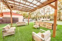 Inviting outdoor area with comfortable seating under a wooden pergola, featuring a barbecue station and lush green lawn.