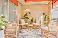 Bright and inviting sunroom with stylish wicker chairs, lush green plants, and textured walls, offering a serene relaxation space.