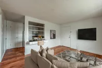 Inviting living room with elegant decor, featuring a sleek wall-mounted TV, contemporary glass coffee table, and plush beige sofa on polished hardwood floors.