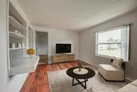 Bright and inviting living room featuring a large window, modern TV setup, and elegant furniture on warm wooden flooring.