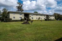 Charming two-story apartment building with well-kept green lawns, picnic table, and grill, ideal for outdoor leisure in a serene neighborhood.