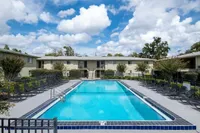 Inviting apartment complex featuring a pristine swimming pool surrounded by sun loungers, under a vibrant blue sky.