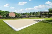 Inviting sand volleyball court surrounded by lush greenery and charming brick buildings under a clear blue sky.