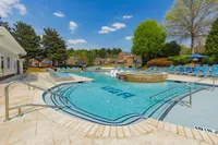 Luxurious outdoor pool area with pristine water, surrounded by vibrant greenery and ample lounging chairs under clear blue skies.