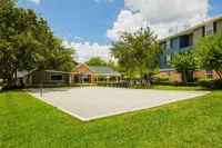 Inviting apartment complex featuring a lush green landscape, volleyball court, and charming residences under a bright blue sky.