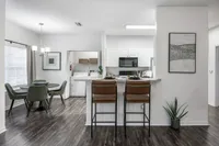 Modern open-concept living space featuring a sleek kitchen, inviting breakfast bar, and elegant dining area with green accent chairs.