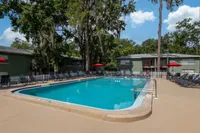 Inviting outdoor swimming pool area surrounded by lush greenery, perfect for relaxation and leisure, featuring comfortable lounge chairs under vibrant red umbrellas.