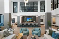Elegant modern lounge area with chic seating, stylish decor, and a sleek kitchen bar under high ceilings.