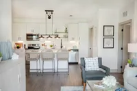 Bright and modern open-concept living space featuring a sleek kitchen with a breakfast bar and wicker chairs, cozy living area with stylish decor, and abundant natural light.