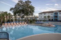 Inviting pool area with comfortable loungers, surrounded by lush greenery and modern apartments in the background, perfect for relaxation and leisure.