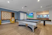 Inviting game room featuring a sleek pool table, comfortable yellow chairs, and a vibrant wall-mounted TV with a tropical beach scene.