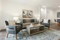 Elegant living room with stylish gray chairs, a cozy sofa adorned with plush cushions, chic abstract artwork, and a modern coffee table on a textured rug.
