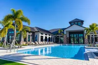 Luxurious resort-style apartment complex featuring a sparkling blue pool, elegant lounge chairs, and towering palm trees under a clear blue sky.