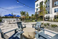 Modern apartment outdoor lounge area with sleek chairs, stylish stone flooring, vibrant blue umbrellas, and lush greenery, offering a luxurious and relaxing environment.