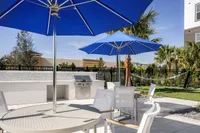 Chic outdoor patio area with blue umbrellas, stylish chairs, a modern barbecue grill, and lush greenery.