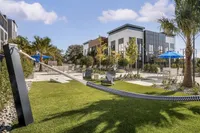 Modern apartment courtyard with lush green lawn, cozy hammock, stylish seating, and vibrant blue umbrellas under a bright sky.