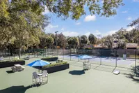 Inviting outdoor tennis court with nearby seating and vibrant blue umbrellas, surrounded by lush greenery for a relaxing atmosphere.