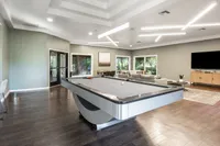 Spacious entertainment room featuring a sleek billiards table, luxurious seating, and modern decor with large windows inviting natural light.