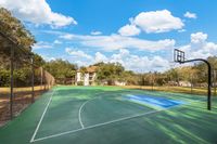 Inviting outdoor basketball court surrounded by lush trees, under a bright blue sky with picturesque clouds.