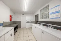 Bright and modern communal laundry room featuring high-efficiency washers and dryers, tiled flooring, and ample folding space.