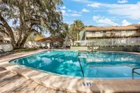 Inviting outdoor pool area surrounded by lush trees and modern apartments, perfect for relaxation and leisure under a bright blue sky.
