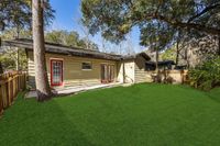 Charming backyard view of a modern house with lush green lawn, surrounded by trees and wooden fencing.