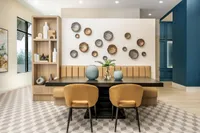 Elegant dining area with modern decor, featuring beige chairs, a stylish black table, and artistic wall accents against a vibrant blue background.