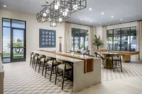 Elegant communal area featuring a stylish bar with high stools, impressive lighting fixtures, modern artwork, and large windows offering scenic views.