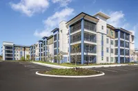 Modern apartment complex with sleek design, featuring spacious balconies and attractive architecture, set against a clear blue sky.
