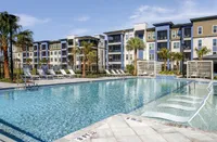 Luxurious apartment complex featuring a sparkling outdoor pool surrounded by sun loungers and lush palm trees.