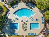 Stunning aerial view of a luxury swimming pool complex with multiple pools, abundant loungers, and lush greenery, perfect for relaxation.
