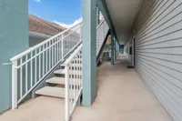 Inviting walkway with clean, modern architecture, featuring light teal walls and white railings leading to elegant apartments.