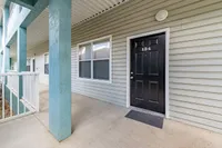 Inviting apartment entrance with black door and modern siding, featuring a spacious and well-lit porch area.