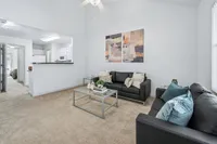 Bright and inviting living room with modern black sofas, plush carpeting, and a sleek glass coffee table, seamlessly connected to the contemporary kitchen.