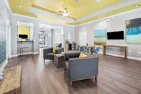Bright and inviting living area with modern grey sofas, elegant wooden tables, and vibrant yellow accents, perfect for relaxation and socializing.