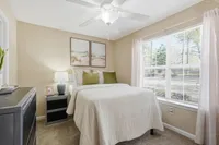Inviting bedroom with soft beige walls, luxurious white bedding, and tranquil artwork, bathed in natural light from a large window, offering a peaceful retreat.