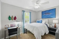 Cozy bedroom featuring a comfortable bed with white linens, a stylish desk setup by the window, and tasteful decor, perfect for relaxation and study.