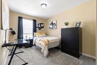 Inviting bedroom with cozy decor, featuring a comfortable bed, modern black dresser, and sleek workspace with ample natural light.
