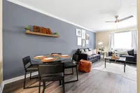 Modern open-concept living and dining area with stylish décor, featuring a sleek glass dining table, cozy leather sofa, and contemporary artwork.