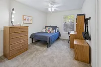Inviting bedroom featuring a cozy bed with vibrant pillows, a stylish wooden dresser, and a functional desk area under natural light.