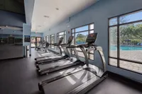 Modern fitness center with state-of-the-art treadmills overlooking a bright outdoor pool area, showcasing a healthy lifestyle within luxurious facilities.