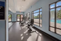 Bright and airy gym room with modern exercise equipment and large windows overlooking a sparkling outdoor pool.