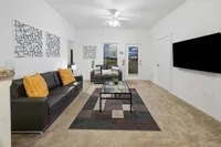 Modern living room with sleek gray sofas, vibrant orange pillows, contemporary wall art, and a stylish glass coffee table on a patterned rug, creating a welcoming and chic atmosphere.