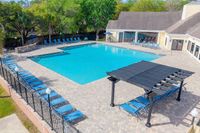 Inviting outdoor pool area with ample seating, shaded pergola, and lush green surroundings, perfect for relaxation and leisure.