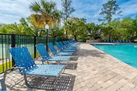 Inviting swimming pool area with stylish blue lounge chairs, surrounded by lush green trees and a bright blue sky.