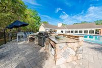 Elegant outdoor patio featuring a stylish barbecue grill and seating area adjacent to a sparkling swimming pool with lush greenery.