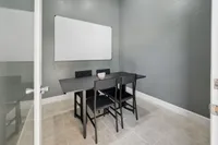 Modern conference room with sleek black table, four chairs, and a whiteboard on a stylish gray wall.