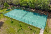 Lush green tennis court surrounded by trees, perfect for outdoor recreation and community sports.