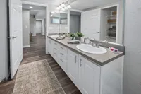 Modern bathroom with dual sinks, elegant cabinetry, large mirror, and sleek flooring. Inviting hallway view adds spacious feel.