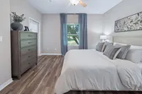 Chic bedroom retreat with modern wood flooring, elegant bedding, and a large window offering serene garden views.